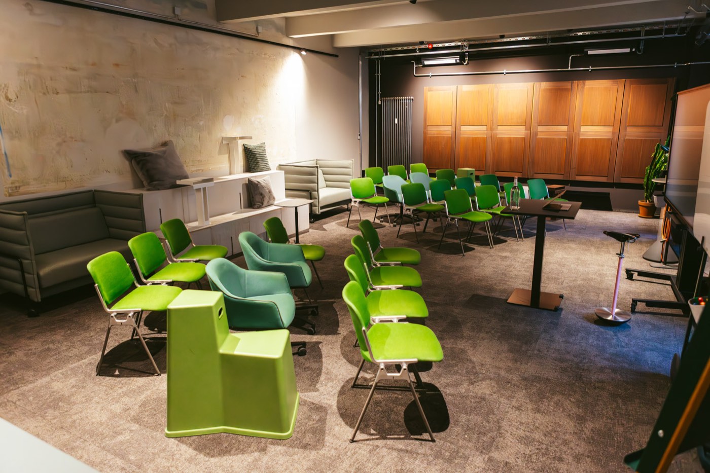Atelier im club199: Stuhlreihen in Grün vor Holzfront, Lounge-Sofas an der Seite